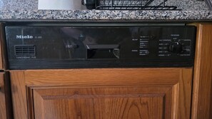 Eine schwarze Miele Spülmaschine mit Bedienfeld, in einer Küche mit Holzschränken und einer Granitarbeitsplatte.