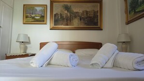 A hotel room with a bed, two bedside lamps, and three framed paintings on the wall. - Charming Glyfada Family Appartment close to the Beach & City center | Quiet Area (Glifada)