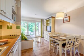 A modern kitchen with a dining area, large windows, and a TV. - Normandy Garden Apartment for 3 (Branville)