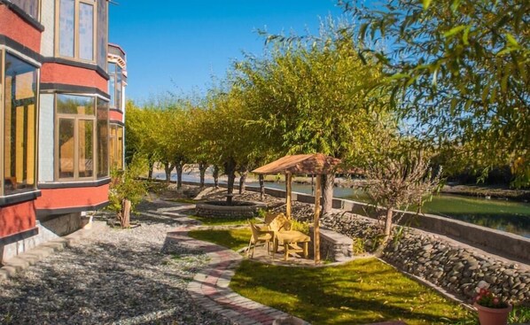 A garden with a pergola, a small table with chairs, and a pathway leading to a building with large windows. - Hotel Nature Residency Leh Ladakh (Leh)