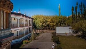 A traditional building with a balcony, a paved pathway, and a garden with trees and shrubs. - Hotel Nature Residency Leh Ladakh (Leh)