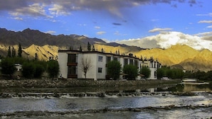 A building with a flat roof, a stone wall, and a reflection in a body of water. - Hotel Nature Residency Leh Ladakh (Leh)