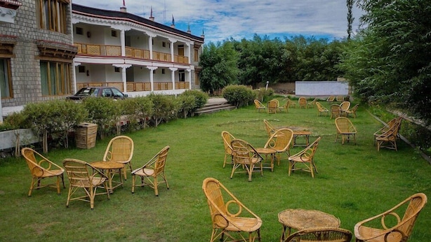 A hotel with a two-story building, a grassy courtyard with wicker furniture, and a parked car. - Hotel Nature Residency Leh Ladakh (Leh)