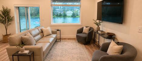 A living room with a sofa, armchairs, a TV, a window with a view, and a small table with a plant.