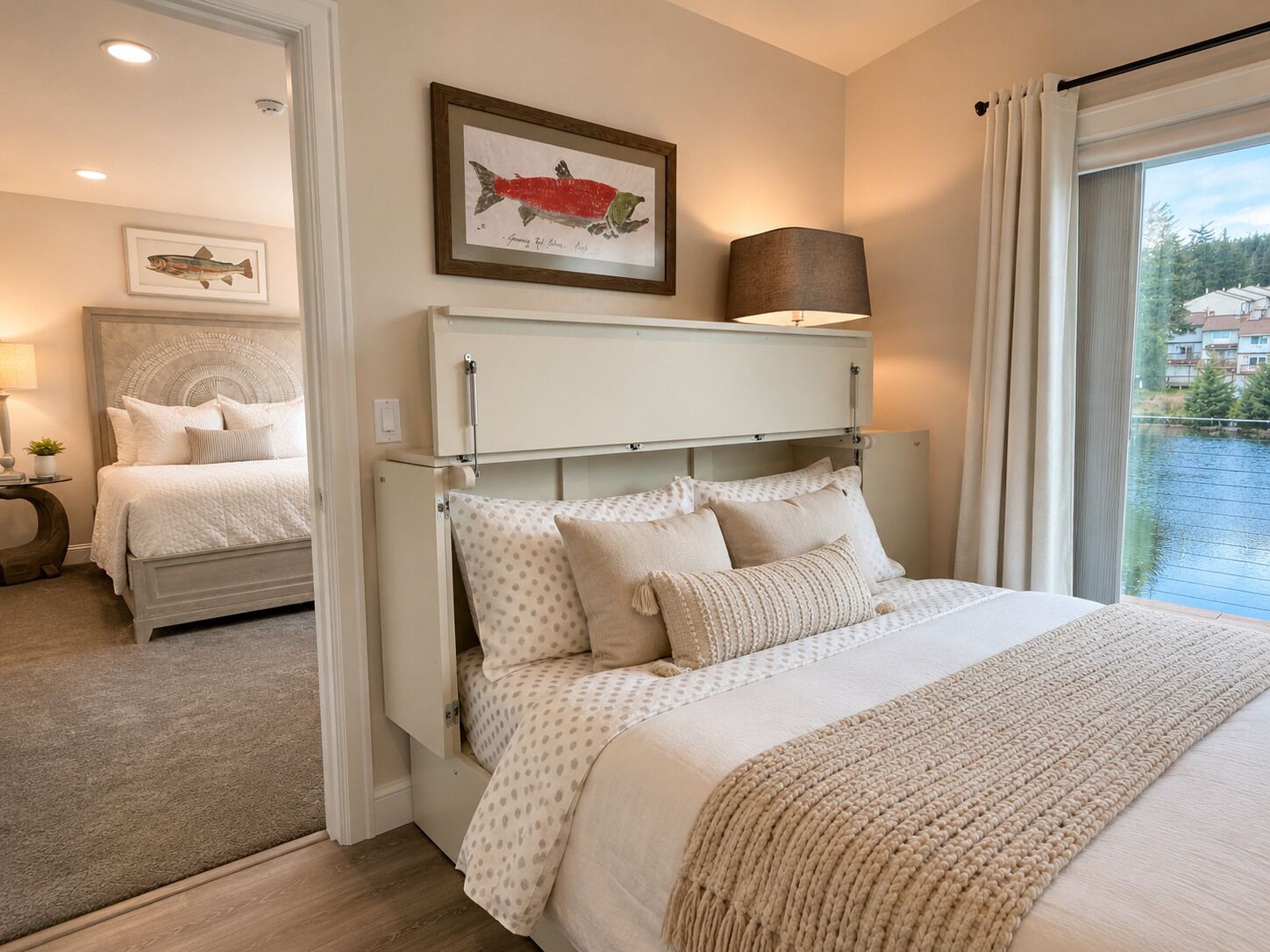 Een slaapkamer met een bed, een nachtkastje, een lamp, een afbeelding van een vis in een lijst en een raam met gordijnen.