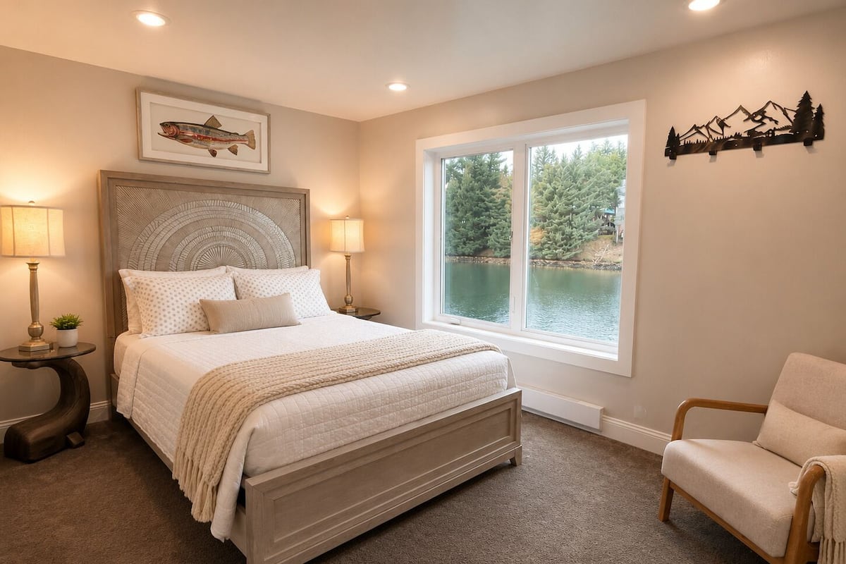 A bedroom with a large bed, two bedside lamps, a window with a view of trees, and a wall-mounted decoration.