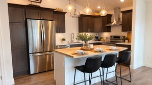 A modern kitchen with a central island, stainless steel appliances, and pendant lighting. - Kodiak Suites (Kodiak)