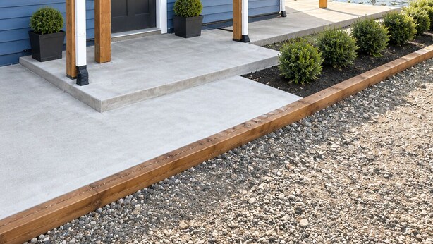 A modern two-story house with a covered porch, a front door, and a small garden area with potted plants. - Kodiak Suites (Kodiak)