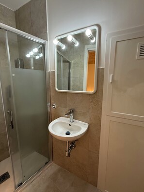 Ein Badezimmer mit Duschkabine aus Glas, einem weißen Waschbecken mit Spiegel darüber und beige gefliesten Wänden.