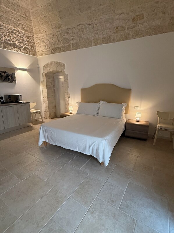 Ein geräumiges Schlafzimmer mit einem großen Bett, einer Steinwand, einem Holzschrank und einem kleinen Tisch mit einer Lampe.
