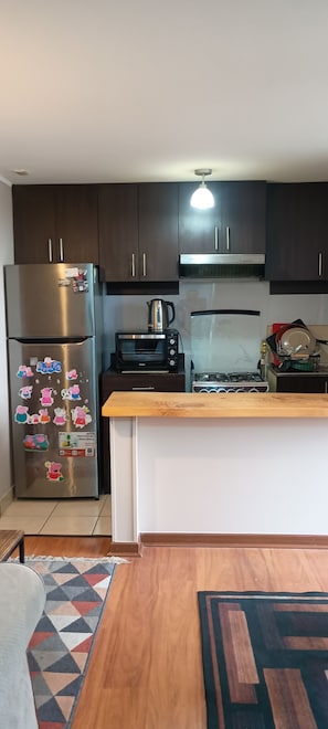 A kitchen with dark cabinets, a stainless steel refrigerator, a microwave, a stove, and a wooden countertop. - Comfortable Apartment for 4, Near Downtown (Temuco)