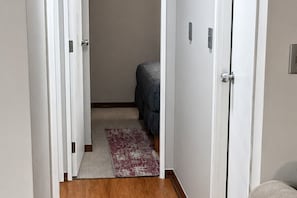 A narrow hallway with a wooden floor, a patterned rug, and a bed with a blue cover. - Comfortable Apartment for 4, Near Downtown (Temuco)