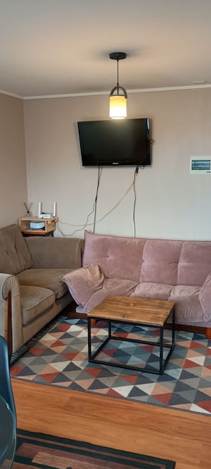 Un salon comprenant un canapé, une table basse, un téléviseur fixé au mur et un tapis à motifs.
