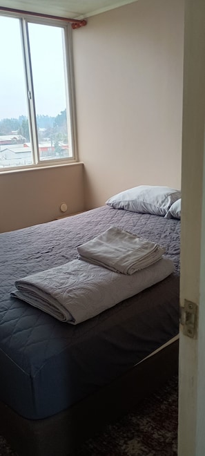 Une chambre avec un lit, une fenêtre et une vue sur les bâtiments environnants.