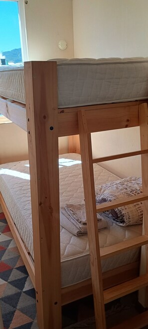 Un lit superposé avec une structure en bois, un matelas et une couverture.
