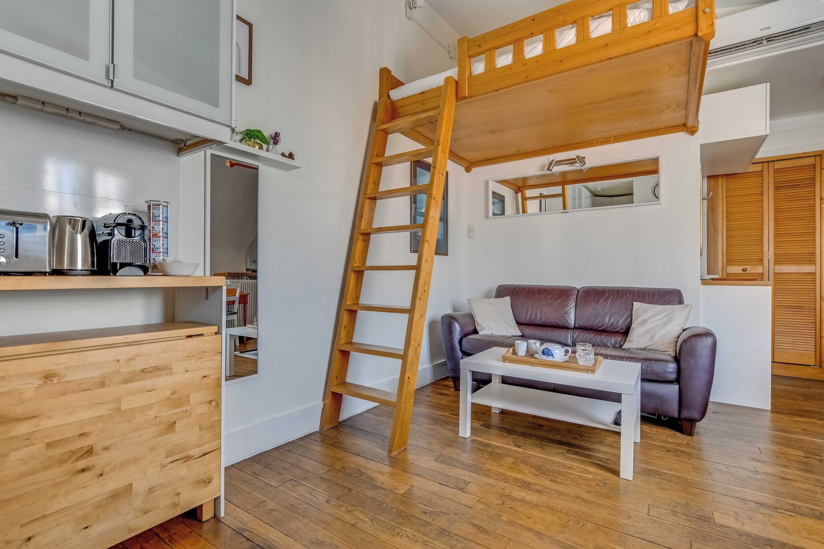 A loft-style room with a wooden ladder, a sofa, a coffee table, and a kitchenette.