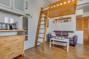 Ein Loft-Zimmer mit Holzleiter, einer Couch, einem Couchtisch und einer Küchenzeile.
