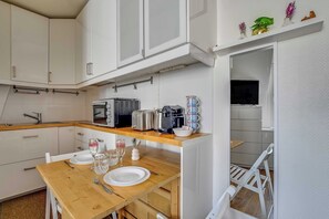 A compact kitchen with white cabinets, a wooden countertop, and a dining area with a table set for two. - Studio 2P Near Tolbiac / Olympiades (Paris)