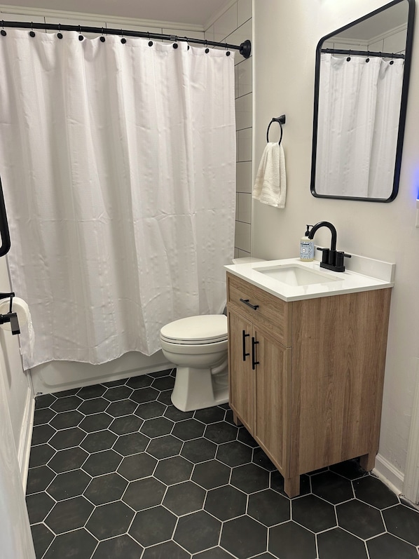 A bathroom with a white toilet, a wooden vanity, a black faucet, and a shower curtain.