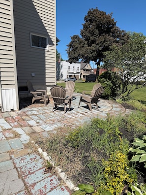 Un patio con sillas Adirondack, un sendero de piedra y una casa al fondo.