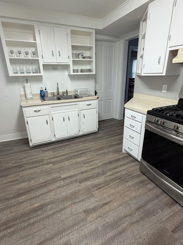 A kitchen with white cabinets, a stainless steel stove, and a wooden floor. - Awesome 5-bedroom house with AC in charming Olean (Olean)