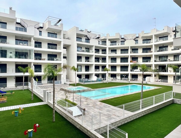 Ein mehrstöckiges Hotel mit einem zentral gelegenen Pool, Außenbereich und Palmen.