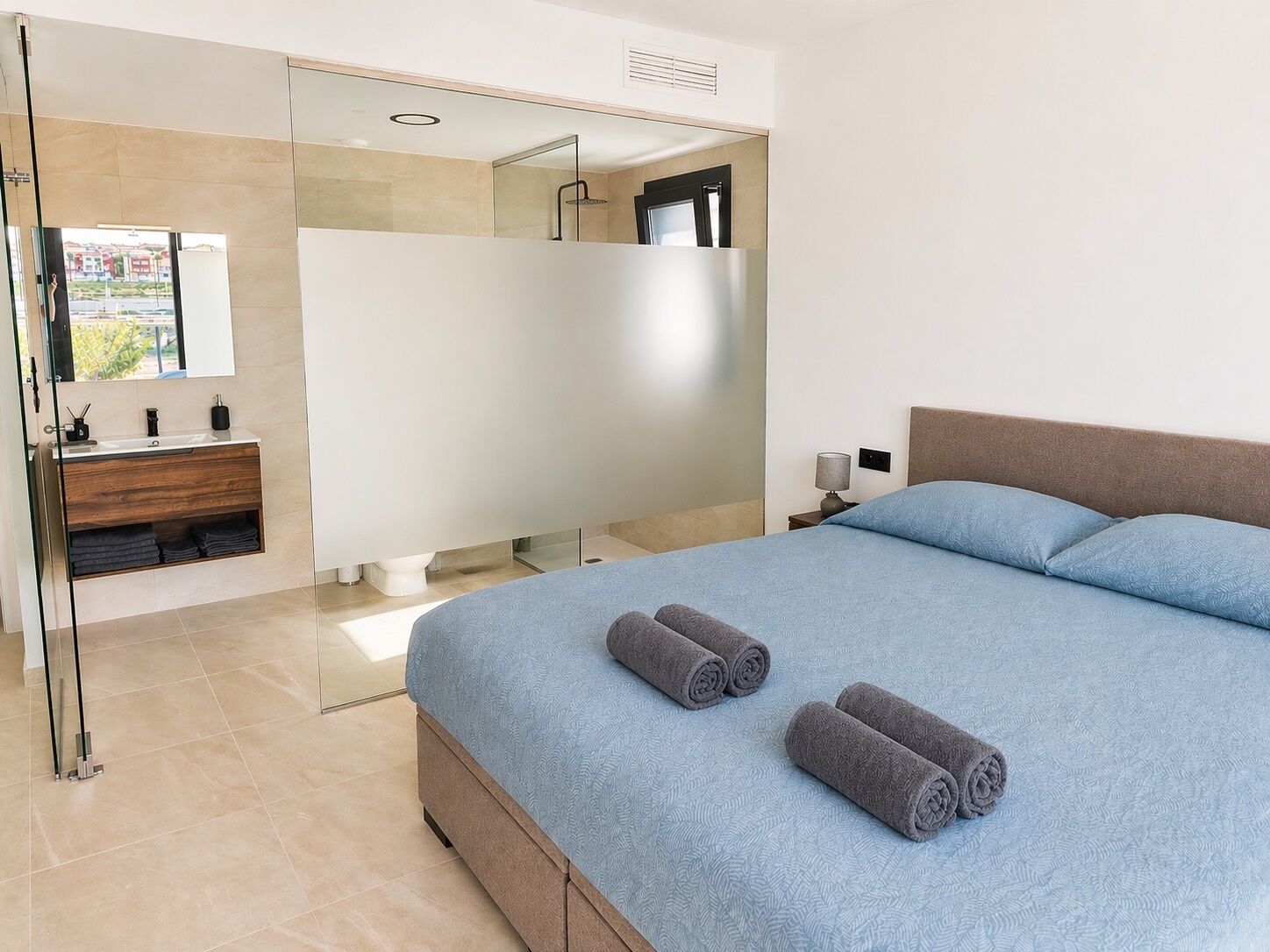 Une chambre moderne avec un grand lit, une salle de bain dotée d’une douche à parois de verre et offrant une vue dégagée sur l’extérieur.