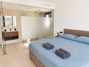 Ein modernes Schlafzimmer mit einem großen Bett, einem Badezimmer mit Duschkabine und Blick ins Freie.