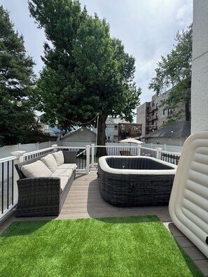 En tagterrasse med en fletsofa, jacuzzi og græsplæne.