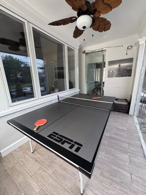 A ping pong table with an ESPN logo, large windows, a ceiling fan, and a cityscape photo on the wall. - 2-bedroom apartment, patio, jacuzzi, 20 min drive to NY. (North Bergen)