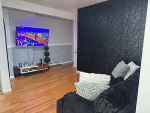 A modern living room with a flat-screen TV, a black sofa, and a decorative wall. - 2-bedroom apartment, patio, jacuzzi, 20 min drive to NY. (North Bergen)