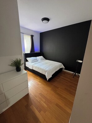Et soveværelse med en seng, en potteplante, et stativ og en loftslampe.