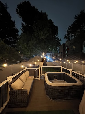 Une terrasse extérieure avec un jacuzzi, un canapé et des guirlandes lumineuses.