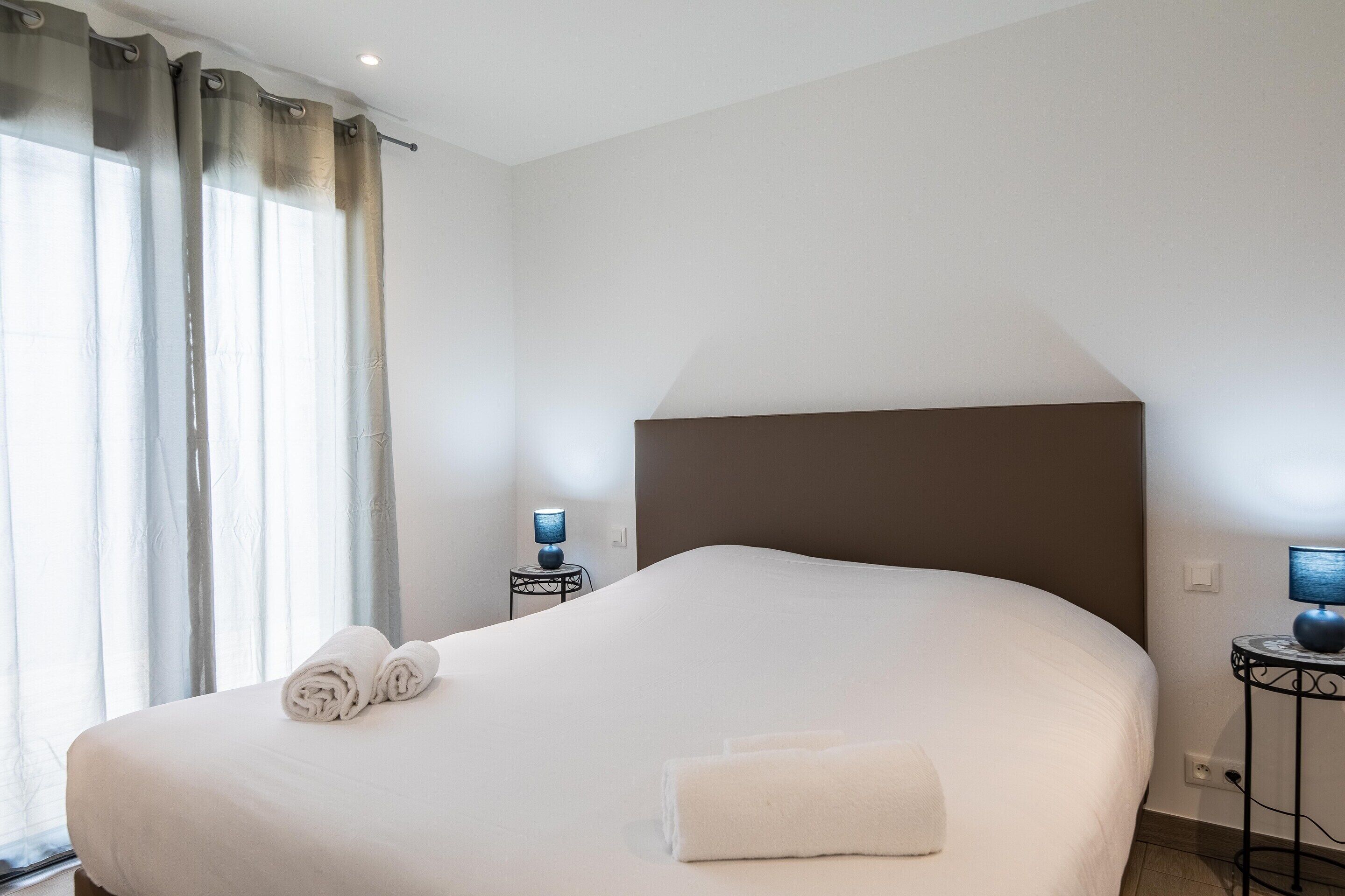 Un lit bien fait, avec des serviettes, une table de chevet avec une lampe et une fenêtre avec des rideaux.