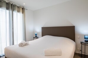 Una cama bien hecha con toallas enrolladas, una lámpara de noche y una mesita con lámpara.