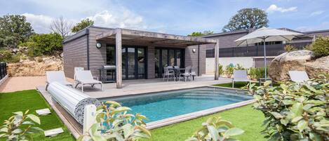 A modern house with a pool, patio with chairs, and a covered outdoor area.