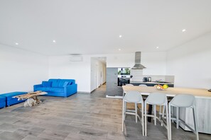 Un espacio habitable moderno con un sofá azul, una mesa de centro de madera, una zona de cocina con una mesa de comedor y sillas, y un sofá gris.