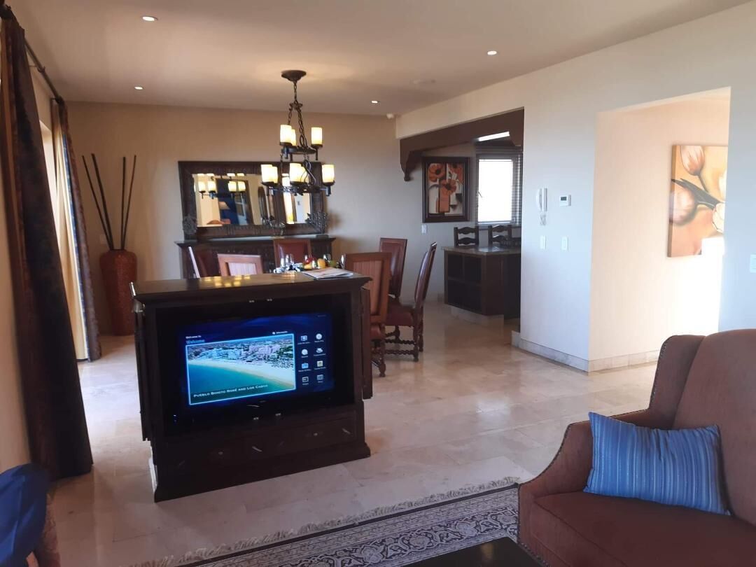 A living room with a flat-screen TV, a sofa, a coffee table, and a dining area with chairs and a chandelier.