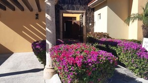 Une entrée d’immeuble avec un arc en pierre, une porte et, au premier plan, de vives fleurs roses.