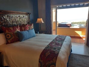 Ett hotellrum med en stor säng, ett nattduksbord, en lampa och utsikt över balkongen.