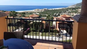 Un balcon avec vue sur la plage, les bâtiments et la végétation.