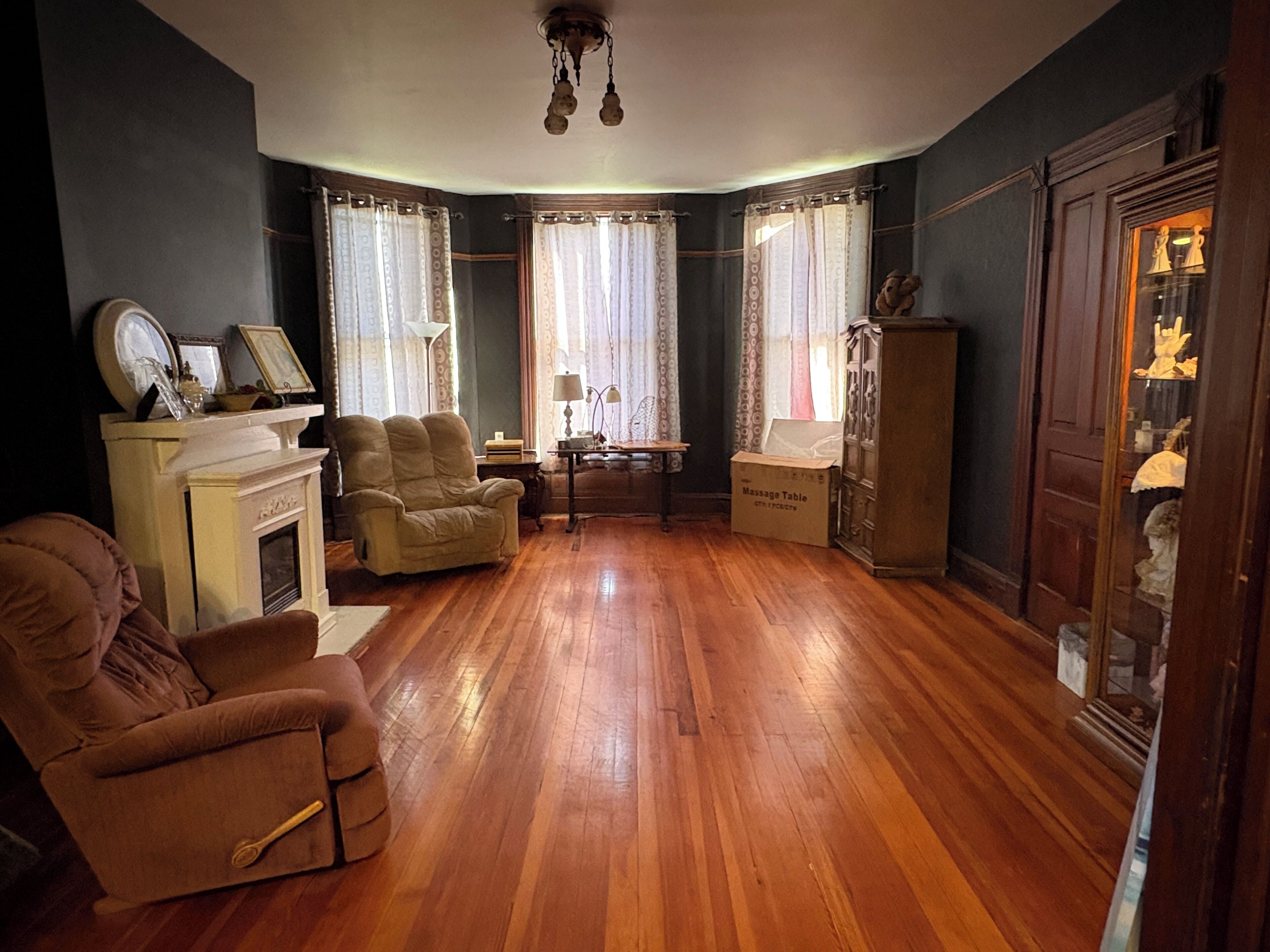 A room with a fireplace, two armchairs, a wooden floor, and a cabinet with glass doors.