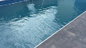 En swimmingpool med en stege, omgiven av en stenmur och ett staket.