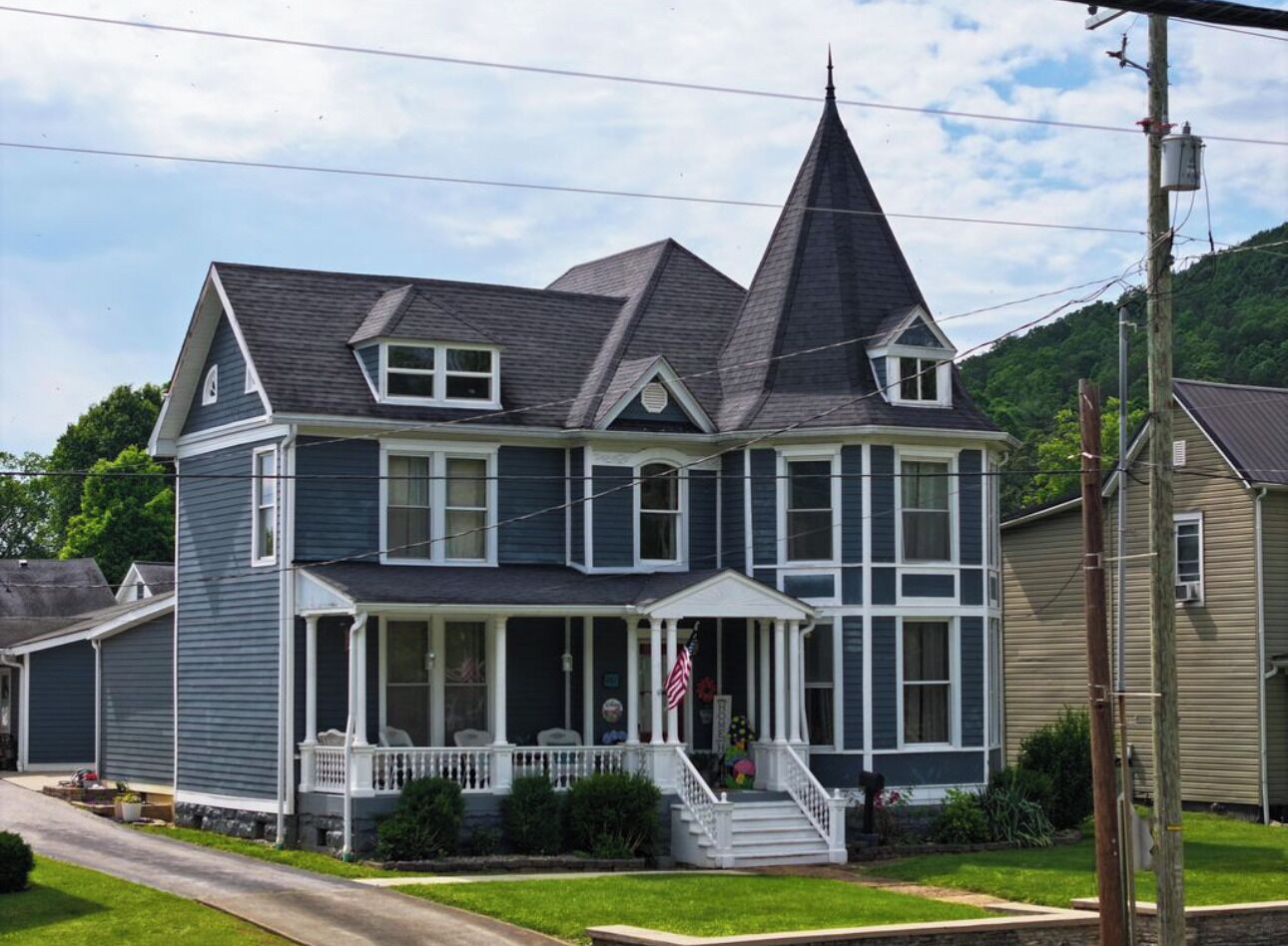 A two-story house with a steeply pitched roof, a front porch, and a small front yard.