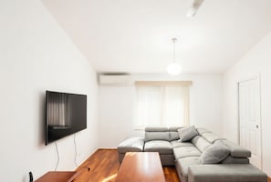 Un salon moderne doté d’un téléviseur à écran plat, d’un canapé d’angle, d’une table basse en bois et d’un luminaire suspendu au plafond.