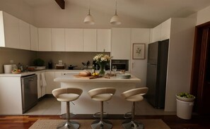 A modern kitchen with white cabinets, a central island with stools, a dishwasher, a refrigerator, and a dining area.