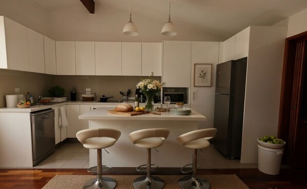 A modern kitchen with white cabinets, a central island with stools, a dishwasher, a refrigerator, and a dining area.