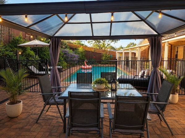 Un patio couvert avec une piscine, du mobilier d’extérieur et une vue sur une maison.