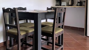 A dining table with four chairs, a flat-screen TV mounted on the wall, and a kitchen area with a microwave, coffee maker, and toaster.