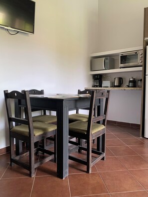 Ein Esstisch mit vier Stühlen, ein an der Wand befestigter Flachbildfernseher und eine Küchenzeile mit Mikrowelle, Kaffeeautomat und Toaster.